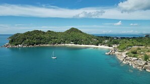 Eine Küstenlandschaft mit einer kleinen Insel, klarem, blauem Wasser und einem Segelboot.