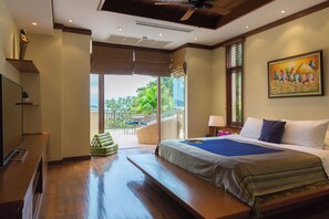 Habitación de hotel con cama, televisor, balcón con vista a la vegetación y un cuadro en la pared.