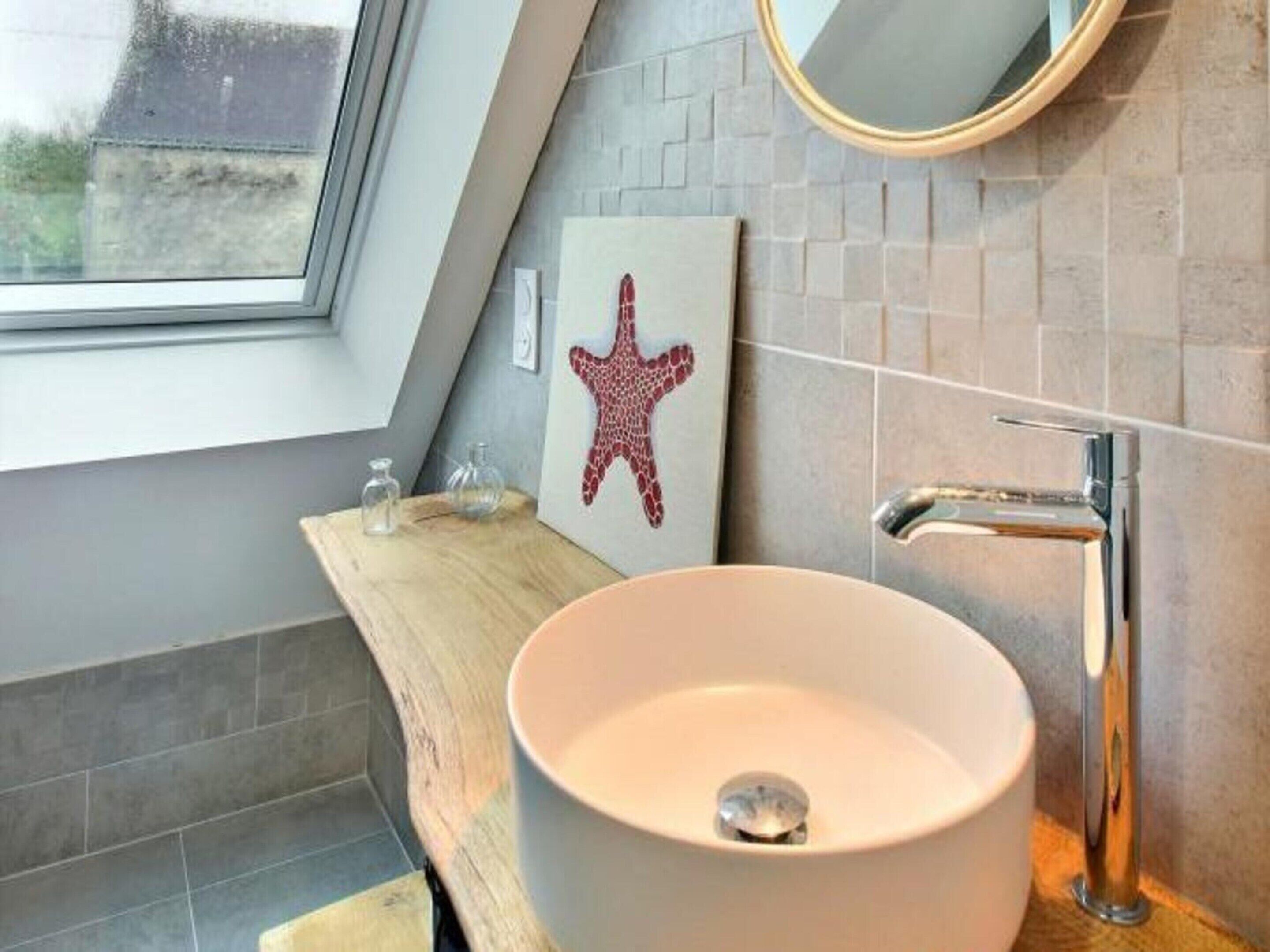 Ein modernes Badezimmer mit einem runden Waschbecken, einer Dekoration mit einem Seestern und einem Fenster.