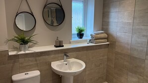 Une salle de bain comprenant des toilettes, un lavabo, deux miroirs, une fenêtre avec une plante et un porte-serviettes.