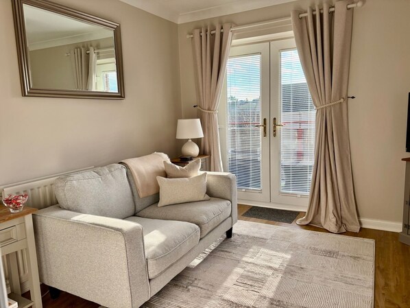 Ein Wohnzimmer mit Sofa, Lampe, Spiegel und Blick durch eine mit Vorhängen drapierten Tür.