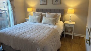 Un lit bien fait, avec une couette matelassée, deux lampes de chevet et deux reproductions encadrées de motifs botaniques accrochées au mur.