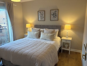 Ein ordentlich bezogenes Bett mit einer gesteppten Daunendecke, zwei Nachttischlampen und zwei gerahmte Pflanzenbilder an der Wand.