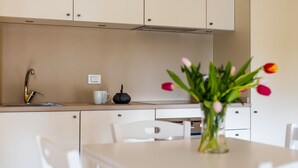 Et moderne køkken med hvide skabe, en stålvask, en hvid bordplade, en sort elkedel og en vase med tulipaner.