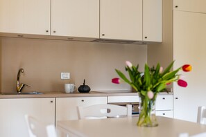 A modern kitchen with white cabinets, a stainless steel sink, a white countertop, a black kettle, and a vase with tulips. - LUXURY GOLF APPARTMENT CLARA (Bogogno)