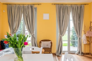 A room with a yellow wall, a wicker chair, a white table, and a window with curtains. - LUXURY GOLF APPARTMENT CLARA (Bogogno)