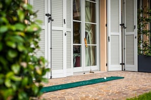 A brick patio with a croquet ball and mallet, white shutters, and a green mat. - LUXURY GOLF APPARTMENT CLARA (Bogogno)