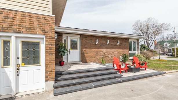 A two-story house with a brick facade, a white front door, and a small porch with red Adirondack chairs.