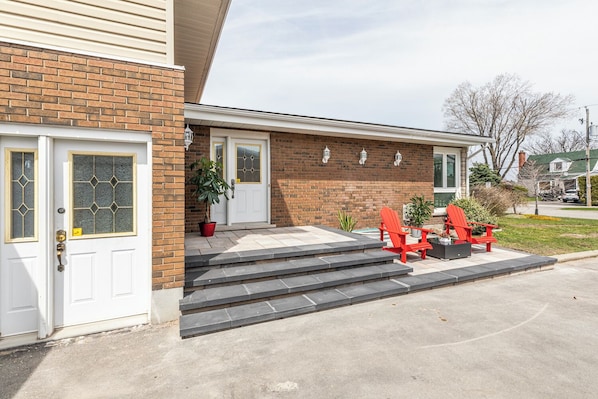 A two-story house with a brick facade, a white front door, and a small porch with red Adirondack chairs.