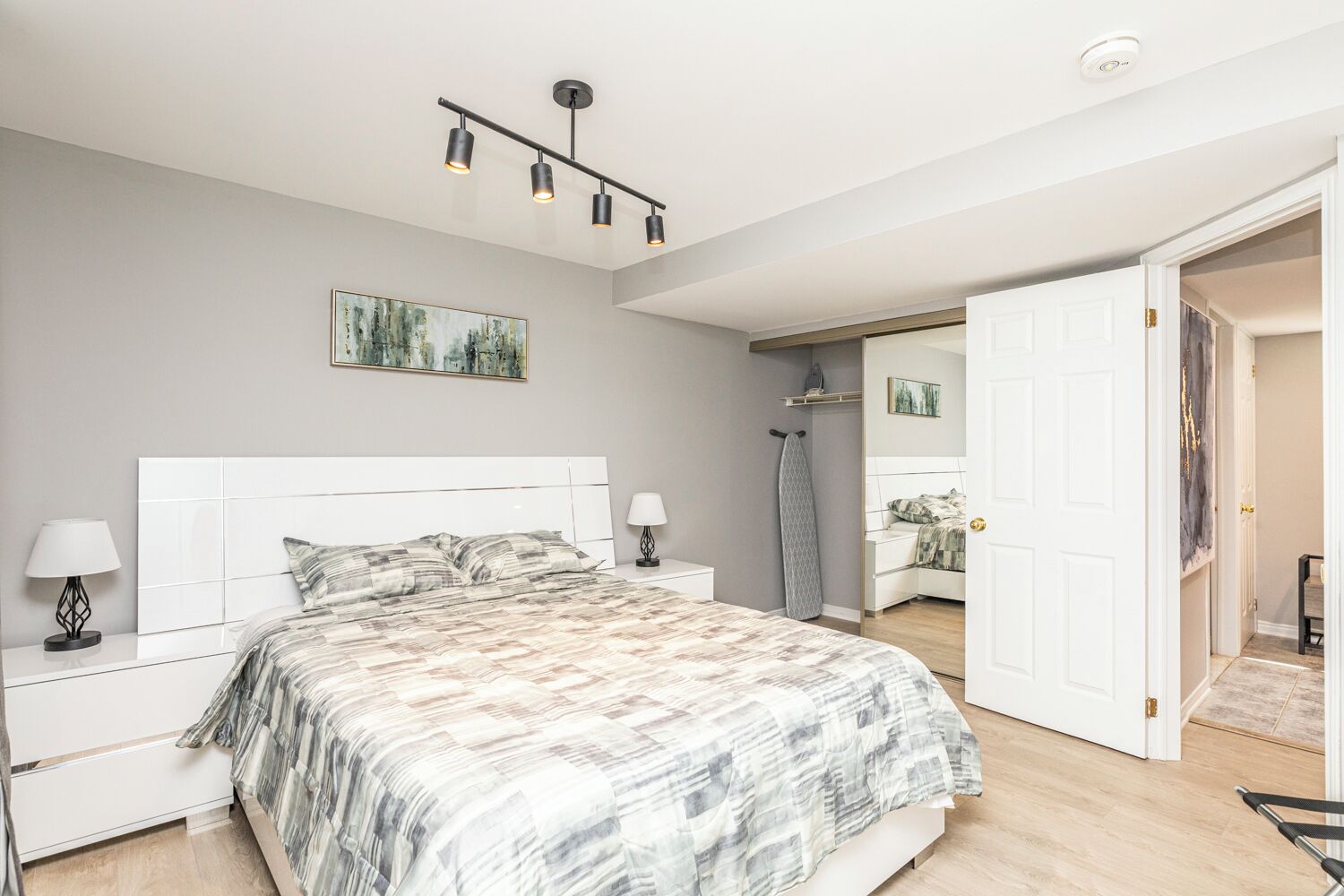A bedroom with a bed, bedside tables, a hanging light fixture, a door, and a painting on the wall.