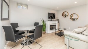 A modern living room with a round dining table, black chairs, a fireplace, a sofa, and a TV mounted on the wall.
