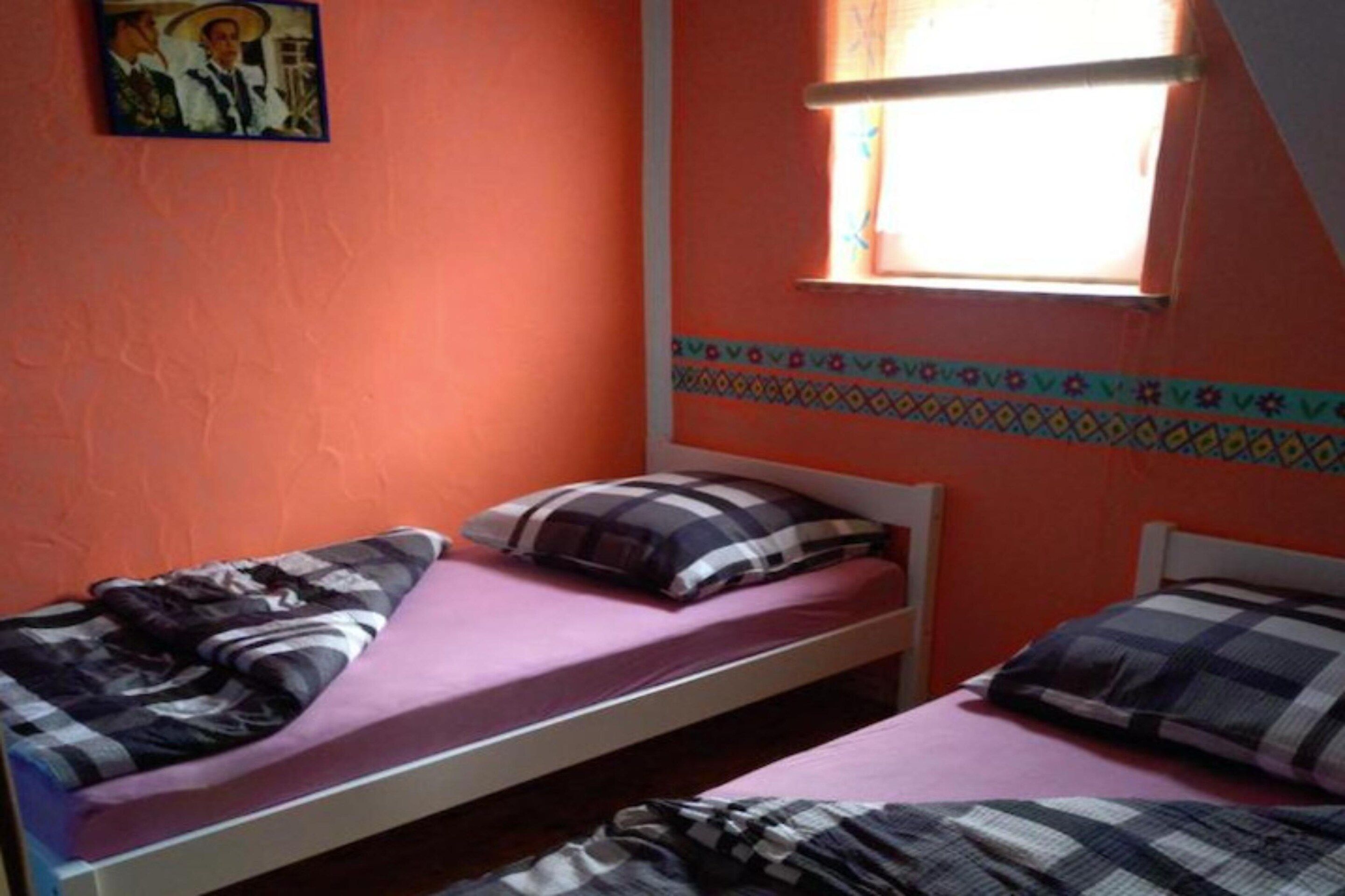 A room with two single beds, each with a pillow and a blanket.