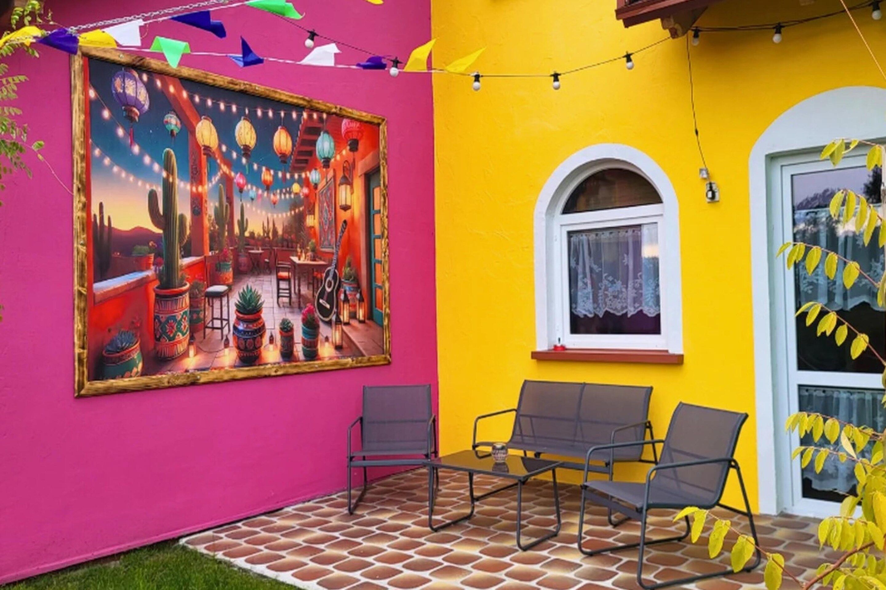 A vibrant patio area with a colorful mural, outdoor seating, and a yellow wall.