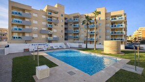 Una piscina rodeada de césped, con un edificio de varios pisos al fondo.