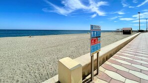 Una playa con un letrero, un paseo marítimo pavimentado y una pequeña estructura que dice 'MASAJES'.