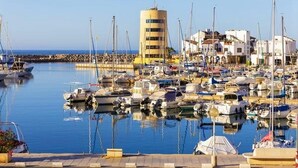 Un puerto deportivo con barcos amarrados, un edificio cilíndrico y un paseo marítimo.
