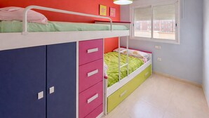 Una cama litera con colchón verde, un mueble cajonera rosa y una ventana con persianas.