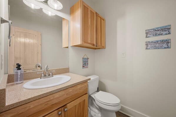 A bathroom with a wooden vanity, a white sink, a toilet, and two motivational posters on the wall. - Waterfront Home Sunset Views, Pool & Pier (Rockport)