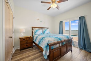 Un dormitorio con cama de madera, una mesita de noche, ventilador de techo, vista al océano y un armario de madera.