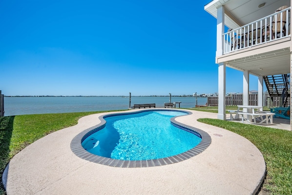 Una piscina con vista al mar, una terraza techada con asientos y una zona verde.