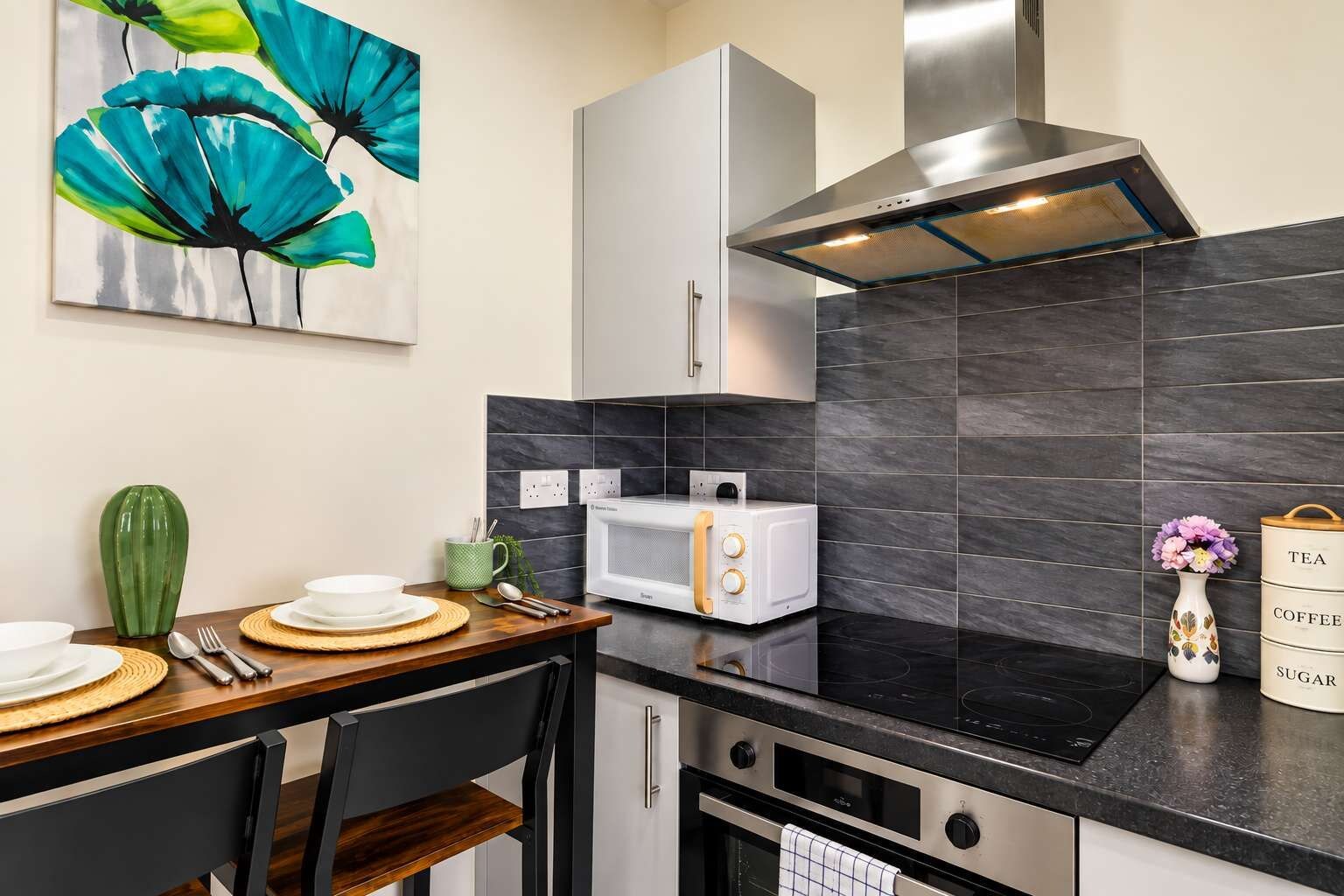A modern kitchen with a microwave, oven, and a stove. There is a dining table with plates and cutlery.