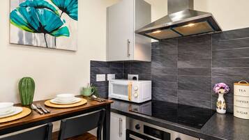 A modern kitchen with a microwave, oven, and a stove. There is a dining table with plates and cutlery.