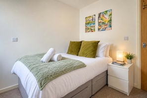 A neatly made bed with a green throw, two pillows, a bedside lamp, and a small plant on a nightstand. - Modern 1BR Apartment, Minutes from Cardiff Centre (Cardiff)