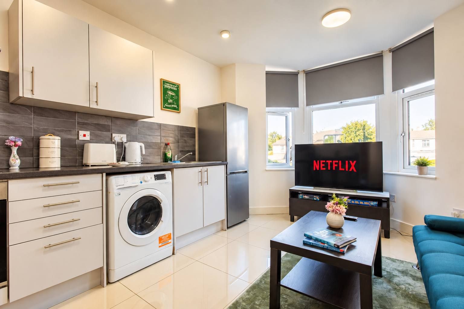 Eine moderne Küche mit Waschmaschine, Kaffeemaschine und einem Fernseher, der 'NETFLIX' anzeigt.