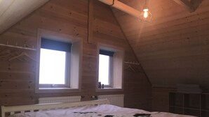 A bedroom with a sloped ceiling, two windows, a bed with a white and black patterned bedspread, a hanging light fixture, and a radiator.