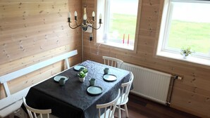 A wooden-paneled room with a table set for four, a chandelier, and a window with a view of a green field.