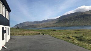 A building with a paved driveway, a fenced grassy area, and a body of water with mountains in the background.
