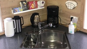 A kitchen with a stainless steel sink, a coffee maker, a kettle, and a shelf with kitchen items.