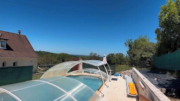 Una piscina en la azotea con cerramiento de vidrio, una terraza cubierta y vistas del paisaje circundante.