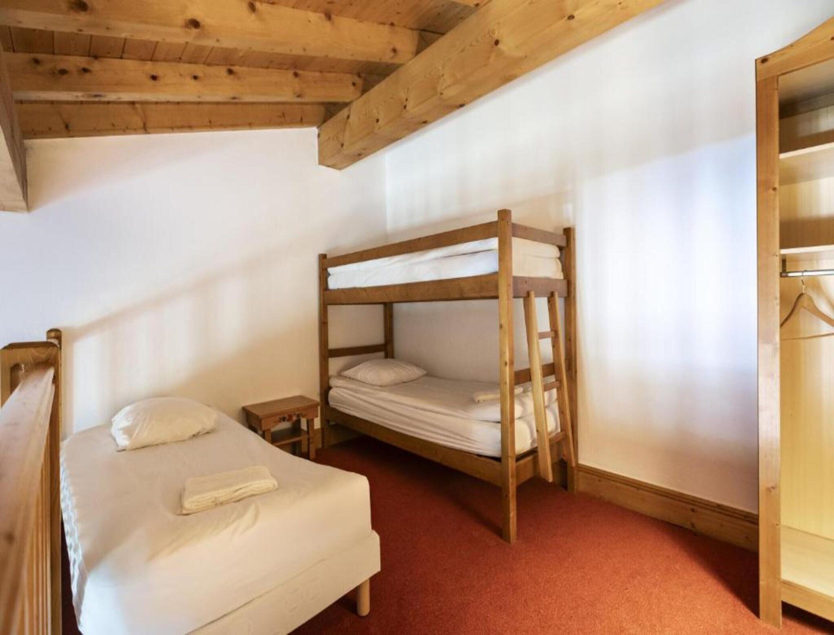 Una habitación con una cama individual, una litera, un armario de madera y una mesita de noche pequeña.