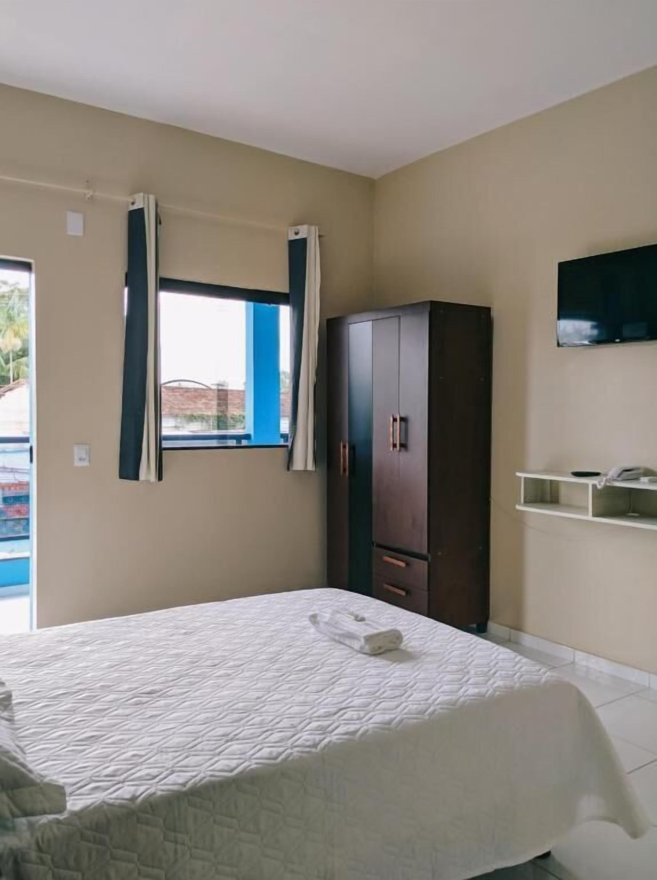 A bedroom with a bed, a wardrobe, a television, and a window with curtains.