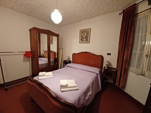 Ein Schlafzimmer mit einem hölzernen Bett, einem Spiegel, einem Nachttisch mit Lampe und einem Fenster mit Vorhängen.