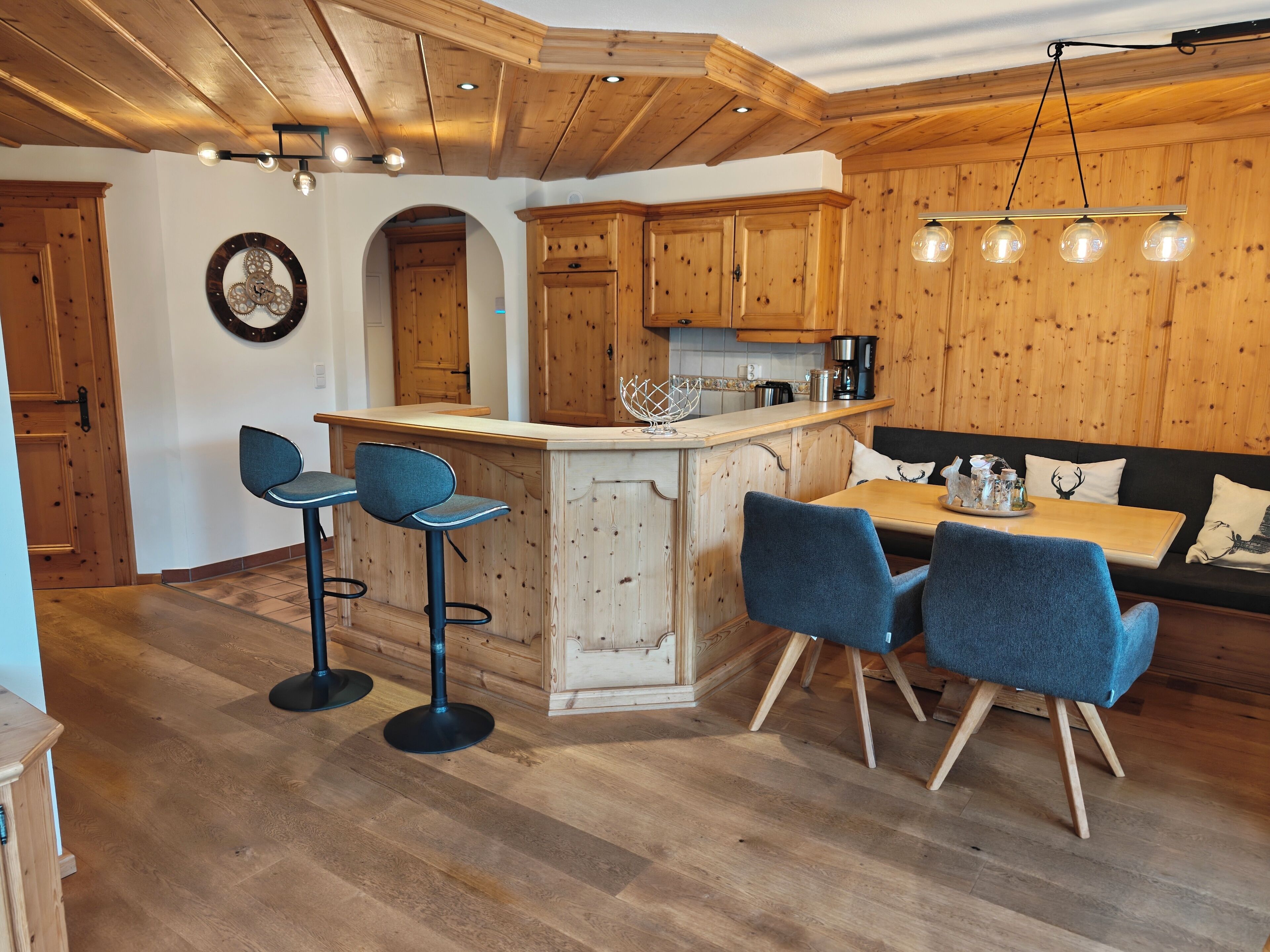 Een houten interieur met een keukeneiland, barstoelen, een eettafel met stoelen en een bank.
