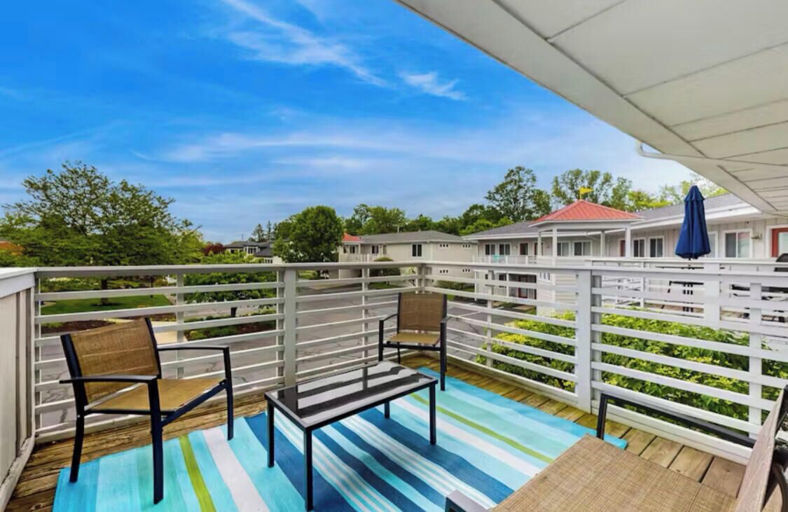 A covered outdoor area with a striped floor, two chairs, a table, and a blue umbrella.