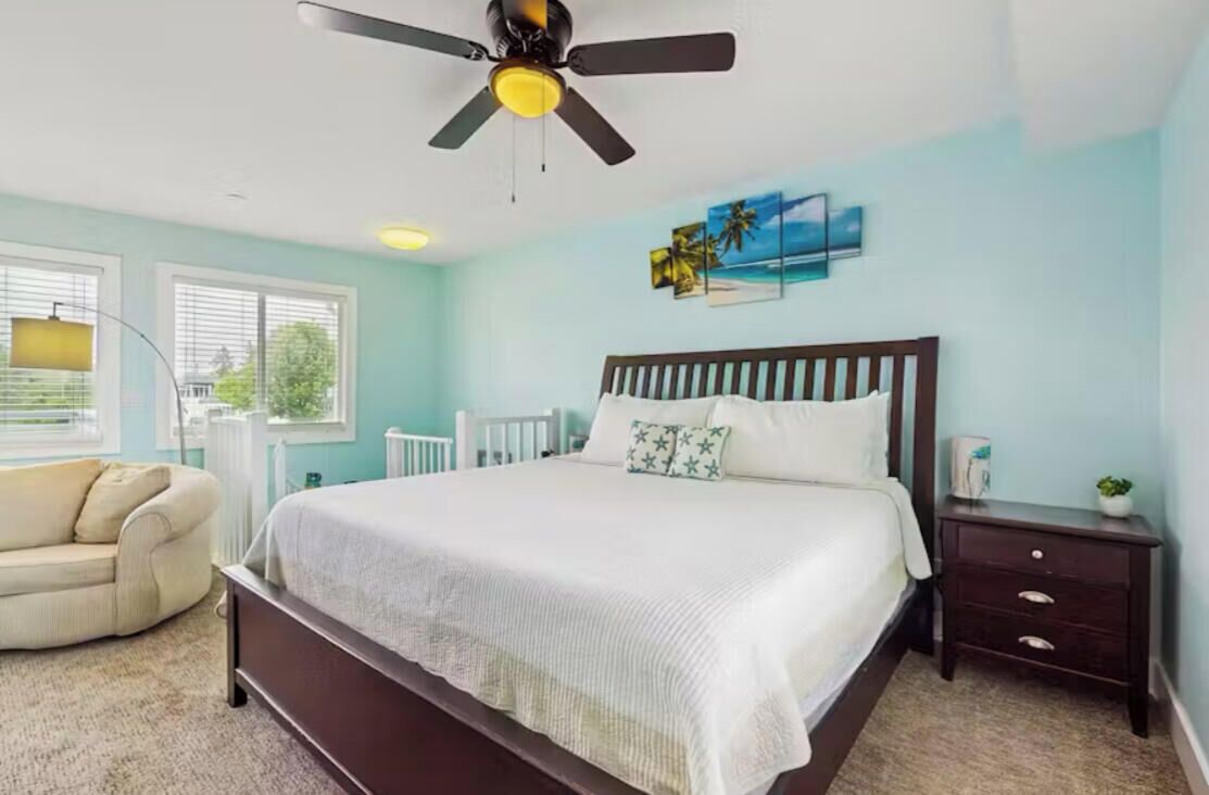 A bedroom with a bed, a ceiling fan, a nightstand, a dresser, and a window with blinds.