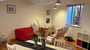 Un coin repas comprenant une table, des chaises, un canapé rouge et une fenêtre avec des stores.