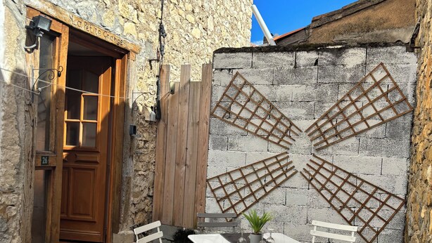 Un bâtiment en pierre avec une porte en bois, une petite table avec des chaises et une plante en pot.