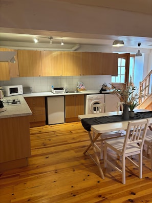 A kitchen with wooden cabinets, a microwave, a toaster, a sink, a dishwasher, and a dining area with a table and chairs.