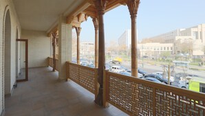 A balcony with wooden columns and a patterned railing, overlooking a street with parked cars and buildings.