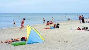 Een strand met mensen die zonnebaden, een tent en mensen die in het water zwemmen.