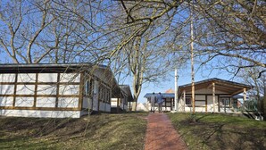 Een pad dat leidt naar een rij gebouwen met een combinatie van moderne en traditionele architectuur, omgeven door bomen en een heldere lucht.