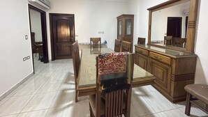 Un coin repas comprenant une table à plateau en verre, des chaises en bois, un chemin de table à motifs, un buffet en bois et un grand miroir.