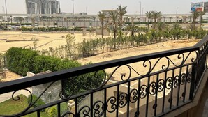 Un balcon donnant sur une plage de sable, des palmiers et des bâtiments situés au loin.