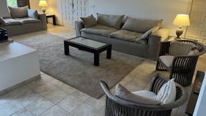 A living room with a sofa, a coffee table, a chair, and a lamp. - "Beautiful villa featuring a large swimming pool and landscaped gardens, privacy. (VC)