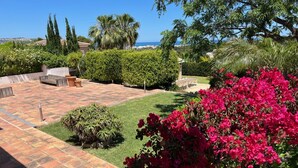 A patio with a tiled floor, a grassy area, and a flowering bush. - "Beautiful villa featuring a large swimming pool and landscaped gardens, privacy. (VC)