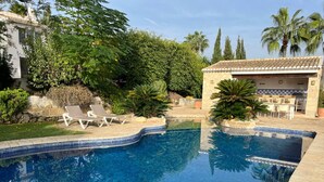 A swimming pool with tiled edges, surrounded by lounge chairs and greenery. - "Beautiful villa featuring a large swimming pool and landscaped gardens, privacy. (VC)